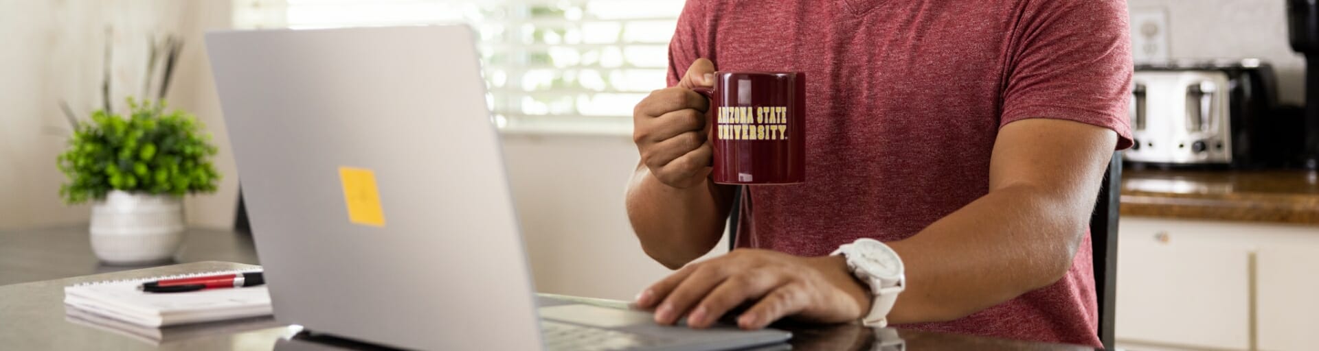 student sitting in front of his computer drinking from an ASU coffee mug